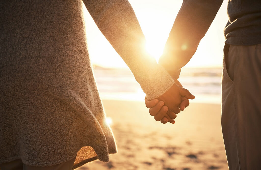 A couple holding hands and walking together towards the sunrise on a beach, a deep bond between two souls.