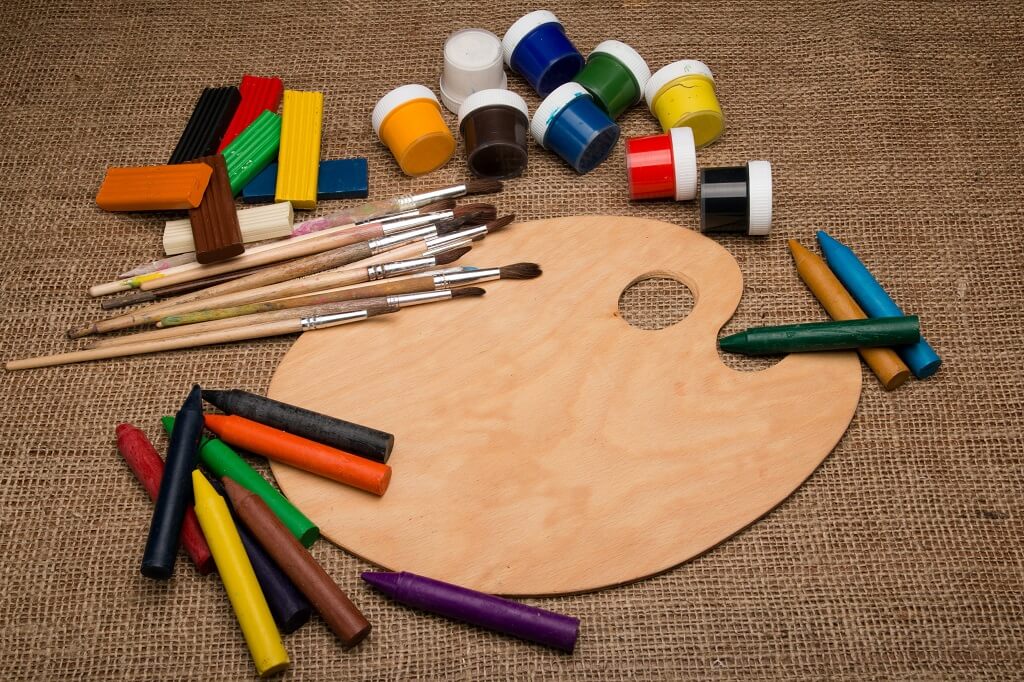 The picture shows how we can play with an oval wooden painter's palette bordered by 
colored blocks, colored paints, colored crayons and paint brushes.