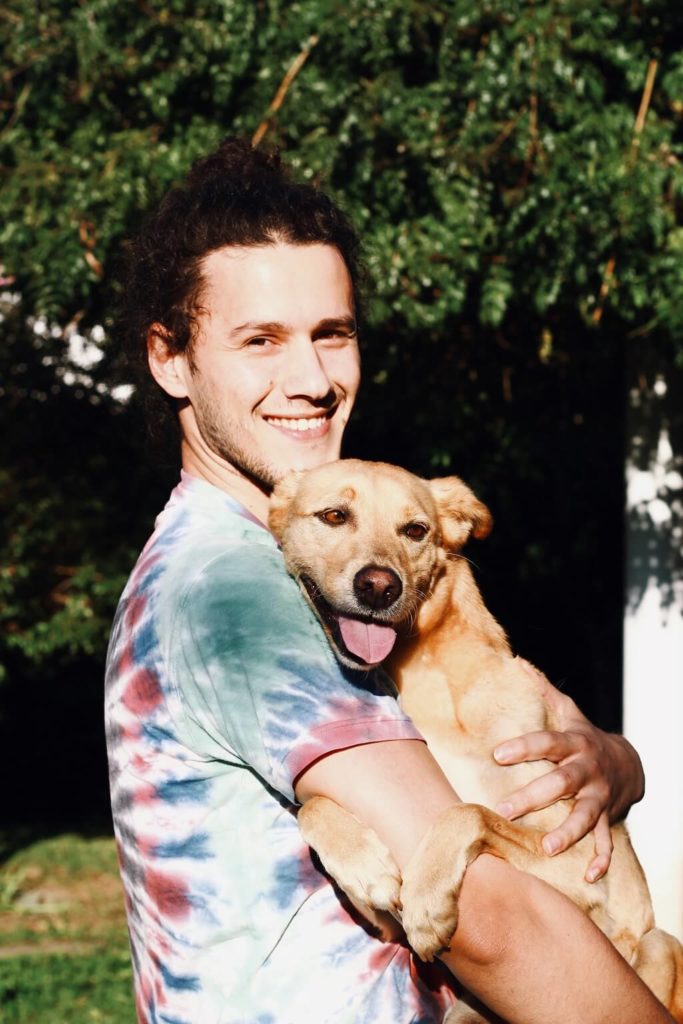 Smiling young man holding a happy dog in his arms and showing us a lovable man.