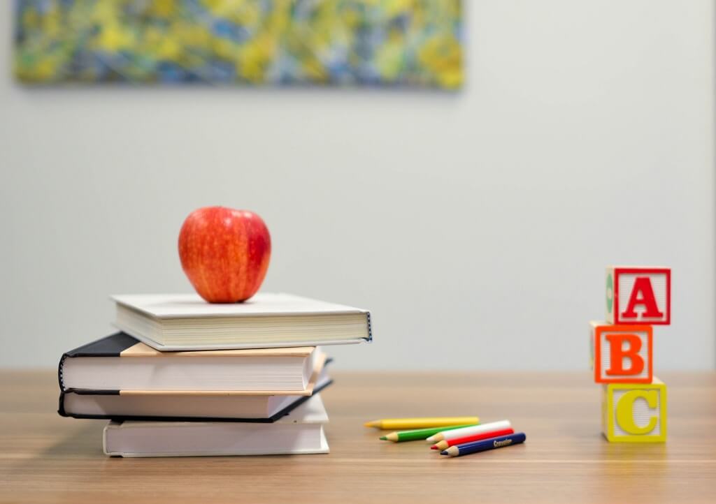  For a course on the lies we tell ourselves, we see an apple, books, colored pencils and blocks on a teacher's desk.