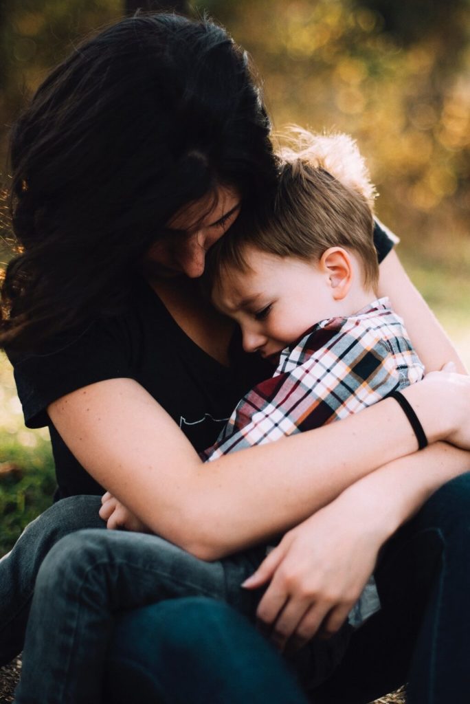 The picture shows a mother holding a little boy  who seems to be in emotional distress.