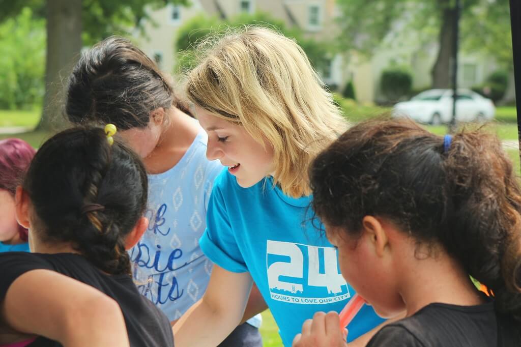 A photo of a young woman encouraging girls in an activity. A person who serves others is capable of loving so is someone to love.