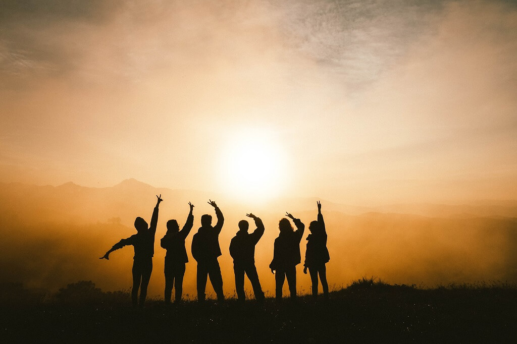 The photo is a silhouette of six persons on top of a mountain, joyfully raising their arms to the sunlight. Is one your true friend?